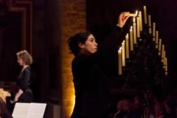 Sarah Charles lights candles in a candelabra on stage in concert